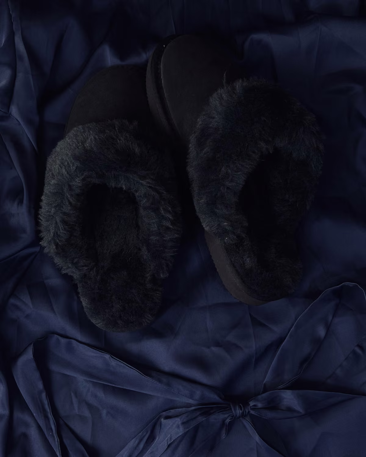 The Elysian in Midnight, charcoal shearling slippers resting on navy satin